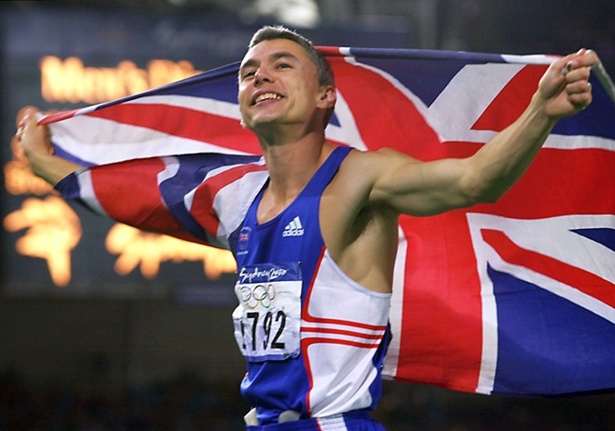 Jonathan Edwards of Britain displays the British flag during the tour of honor after winning the Olympic men's triple jump gold medal 25 September, 2000 in the Sydney Olympic Games. AFP PHOTO/Eric FEFERBERG